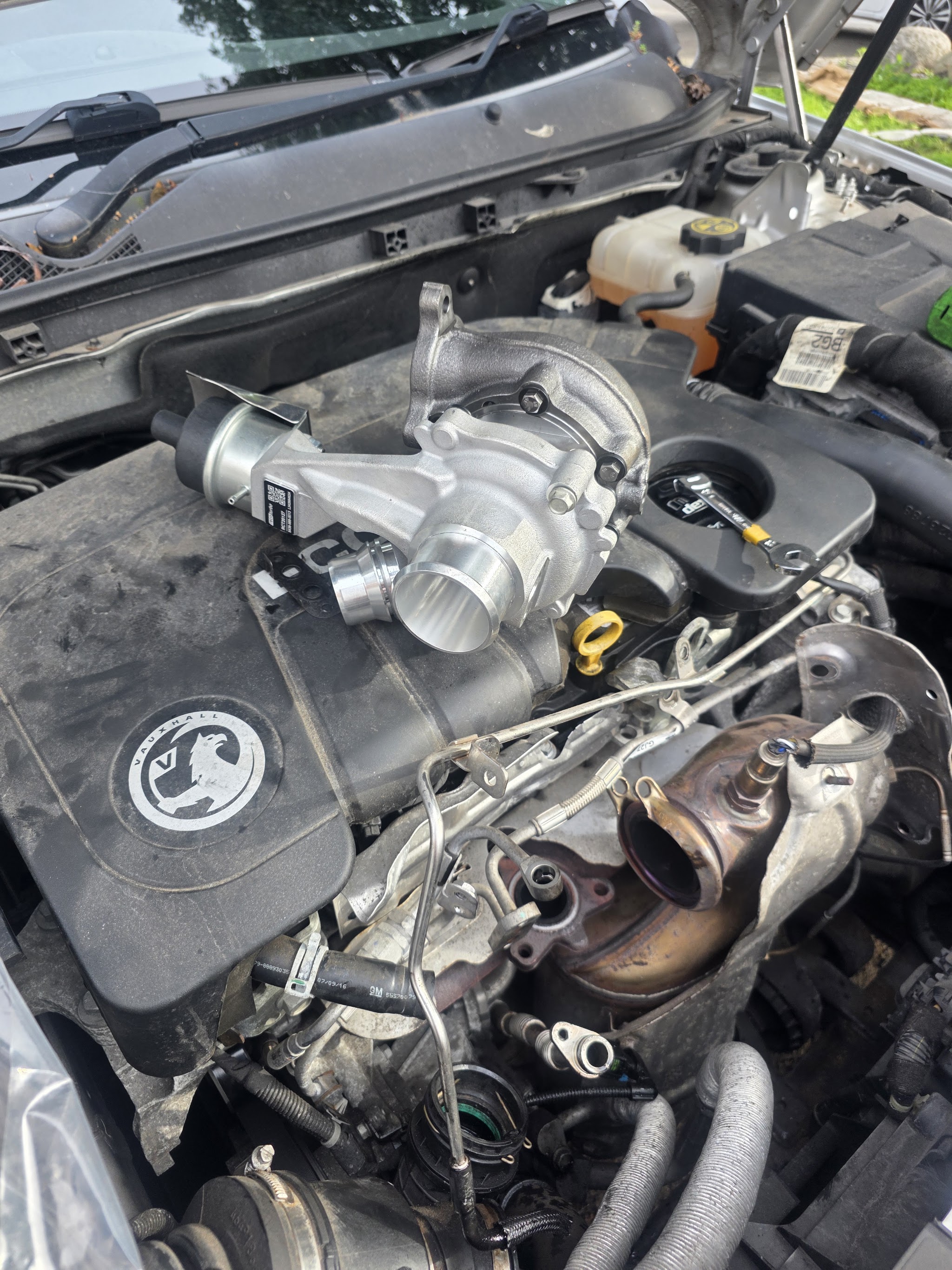A new turbocharger sitting on a Vauxhall engine cover with a spanner beside it